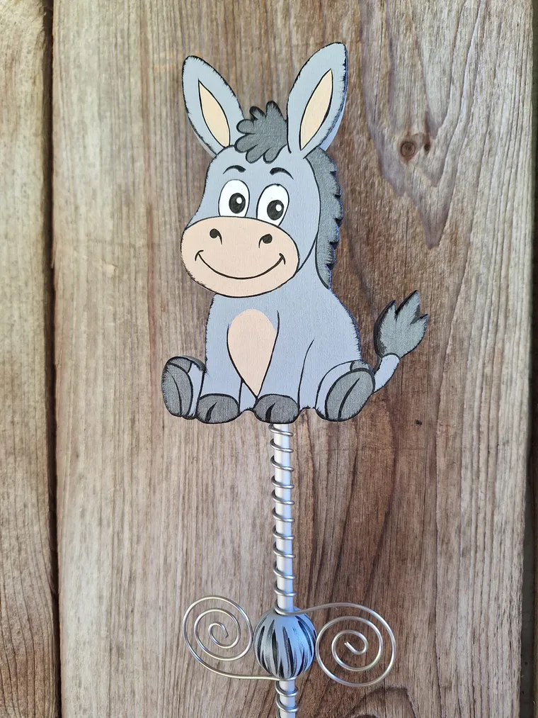 Handbemalter grauer Esel als Gartenstecker vor einer rustikalen Holzwand.