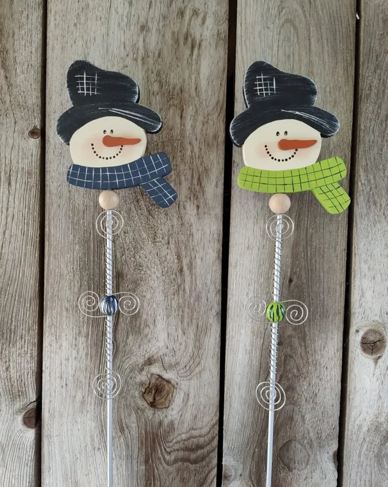Zwei handbemalte Schneemann-Gartenstecker vor einer rustikalen Holzwand.