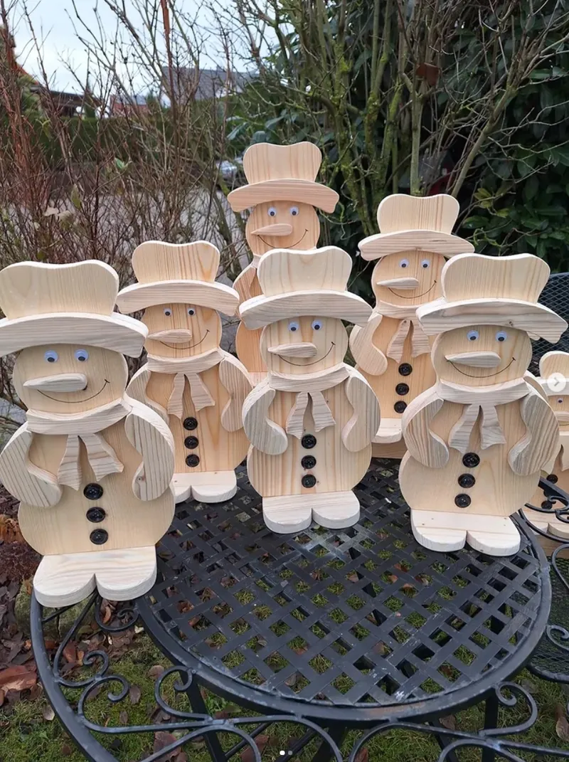 Mehrere naturfarbene Holz-Schneemannfiguren auf einem Gartentisch.