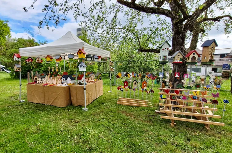 Marktstand im Grünen mit Vogelhäusern, Gartensteckern und Holzdekoration unter einem weißen Pavillon.