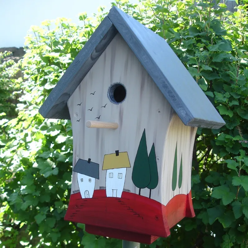 Holz-Vogelhaus mit handgemalter Landschaft, Häusern und Bäumen im Garten.